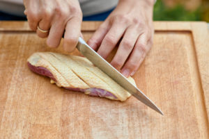 Frauenhände mit Kochmesser ritzen die Haut einer Entenbrustein, Holzbrett Frauenhände mit Kochmesser ritzen die Haut einer Entenbrustein, Holzbrett